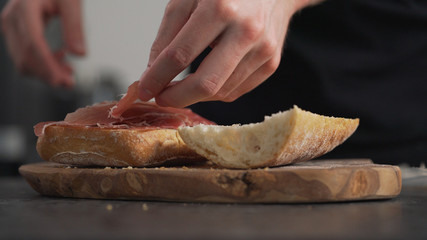 man add prosciutto on ciabatta on olive board