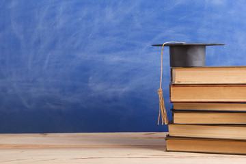 Graduation cap with books on the chalkboard background in the auditorium