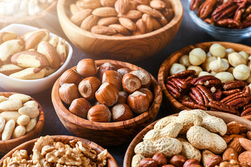 Mix nuts in wooden bowls on dark stone table. Almonds, pistachio, walnuts, cashew, hazelnut.