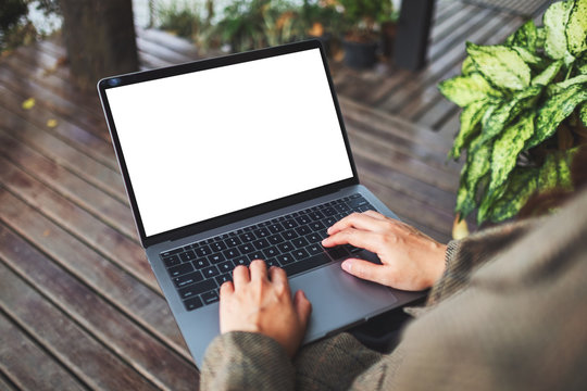 Mockup image of a woman using and typing on laptop computer with blank white desktop screen in the outdoors