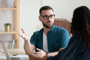 Thoughtful young businessman in glasses discussing project with biracial colleague.
