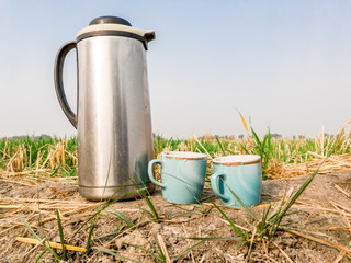 closeup of a pair of  blue cups of coffee and thermos kept outside in the agriculture  fields 