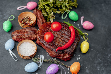 Grilled festive Easter steak with spices and colorful eggs. Easter bunny on stone background 