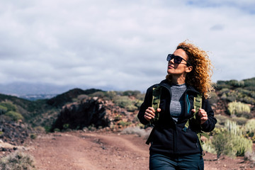 Happy independent beautiful adult caucasian woman in trekking outdoor leisure activity enjoying the nature - modern active people walking with backpack at the mountain