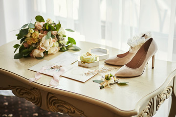 bridal accessories such as shoes, bouquet , ring and  invitation cards lie on a table