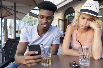 angry jealous young female as her boyfriend uses his phone
