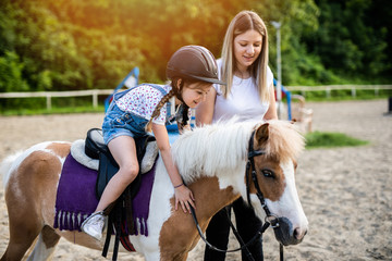 Cute little girl and her older sister enjoying with pony horse outdoors at ranch..