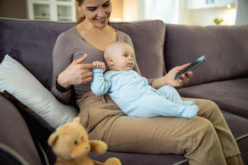Happy young lady sitting with baby and using mobile phone