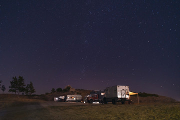 Many motorhome vehicles parked on the beach in night time. Dark starry sky with shining stars. Camper lifestyle