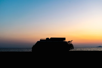 Motorhome silhouette on the beach in the sunset Beautiful orange sky color and calm sea in the background. Camper van lifestyle