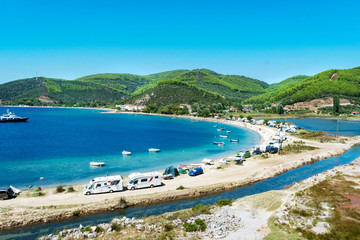 Fototapeta na wymiar View on famous Greek bay with many recreational vehicles parked around the beach and turquoise blue water. Perfect vacation place for camping lifestyle.