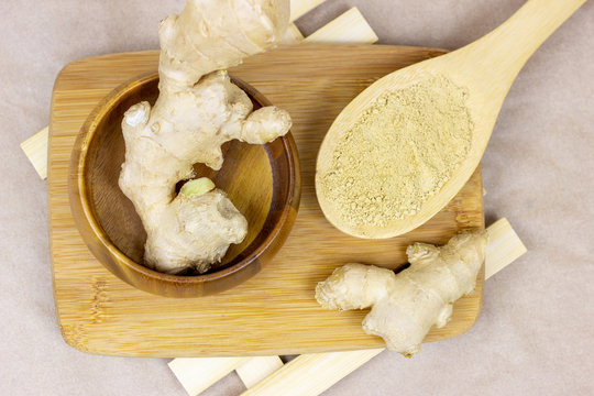 Fresh raw yellow ginger root with ground dry powder in wooden spoon and on wood background.