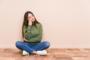 Young caucasian woman sitting on the floor isolated who feels sad and pensive, looking at copy space.