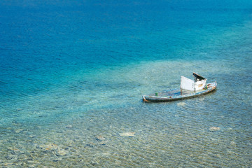 Old forgotten wooden boat rotting in the shallow turquoise waters of the bay. Transparent blue water with rocks on the bottom.