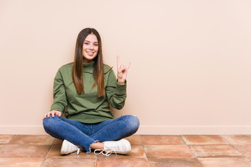 Young caucasian woman sitting on the floor isolated showing a horns gesture as a revolution concept.