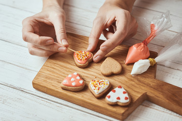 Decorating gingerbread cookies with icing. Woman hand decorate cookies in shape of heart, closeup