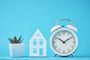 White retro alarm clock and miniature house on the blue backgroumd