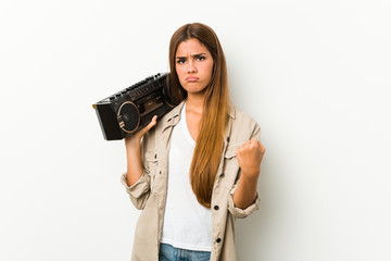 Young caucasian woman holding a guetto blaster showing fist to camera, aggressive facial expression.