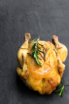 Roasted poussin with rosemary on black stone background