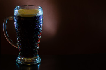 A misted glass of dark beer on a dark background. Close-up, mock-up.