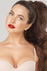 Fototapeta premium Close up portrait of attractive sexy woman with red lips posing looking at camera. Face of beauty fashionable girl in nude bra and luxury makeup isolated at white studio background
