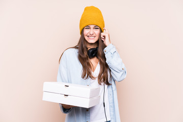 Young caucasian woman holding pizzas isolated covering ears with hands.