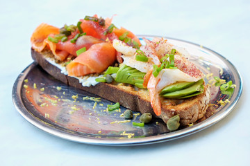 Close up of shot of toasted sandwich with smoked salmon, avocado, shrimp, cream cheese, olive paste and capers. Delicious seafood bruschetta with various ingredients. Top view, copy space, background.