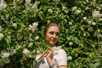 Beautiful girl is walking in the spring park near the trees in bloom. Spring season, sunny weather.