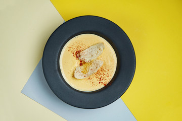 Cheese cream soup in a black bowl with crackers, fried bread and spicies. Tasty food for lunch. colored background