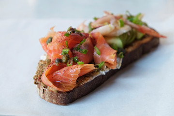 Close up of shot of toasted sandwich with smoked salmon, avocado, shrimp, cream cheese, olive paste and capers. Delicious seafood bruschetta with various ingredients. Top view, copy space, background.