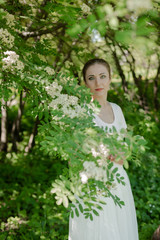 Beautiful girl is walking in the spring park near the trees in bloom. Spring season, sunny weather.