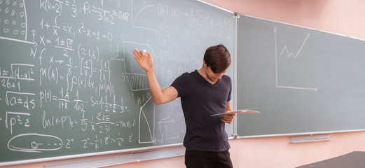 young student in university standing next to the blackboard and thinking at the maths equation