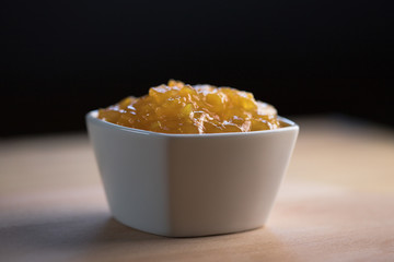 Apricot jam in a white bowl lying on a wooden table close-up shot dark background space for text