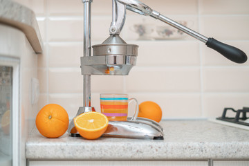 the steel metal manual press juicer with cut oranges and glass on the kitchen table at home