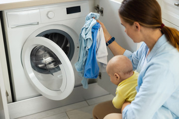 Young mom staying with her baby near washer
