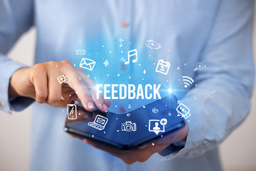 Businessman holding a foldable smartphone with FEEDBACK inscription, social media concept