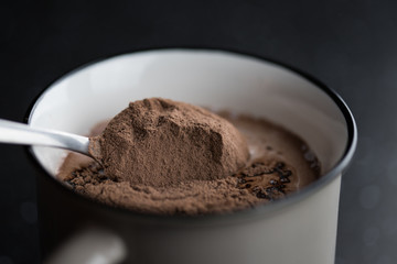 A spoonful of cocoa poured into the milk close-up shot