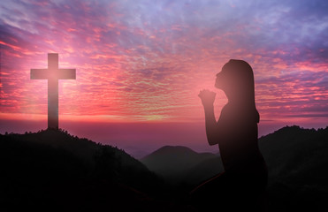 Silhouette of woman kneeling and praying tp god over beautiful sunrise