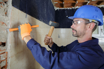 male builder using hammer chisel on interior wall
