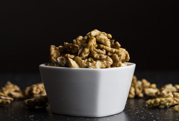 Peeled walnuts lying in a white bowl dark background warm light a healthy snack