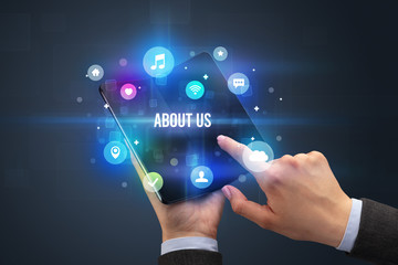 Businessman holding a foldable smartphone with ABOUT US inscription, social media concept