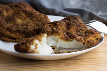 A close-up shot of a breaded fish lying on a white plate on a wooden table
