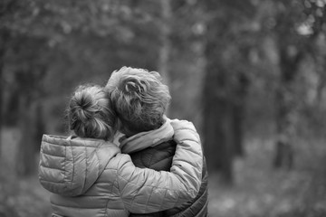 Mom and daughter hug each other standing back in park monochrome black and white