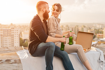 Cheerful couple with beer dating on rooftop