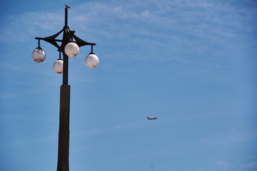 The lamppost looking at the plane in blue sky