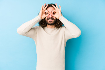 Young long hair man isolated on a blue background showing okay sign over eyes