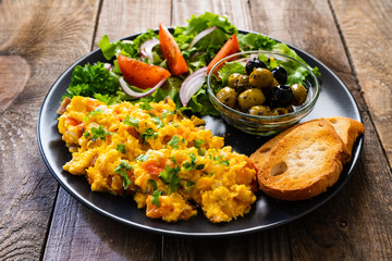 Breakfast - scrambled eggs with vegetables and toasted bread on wooden background