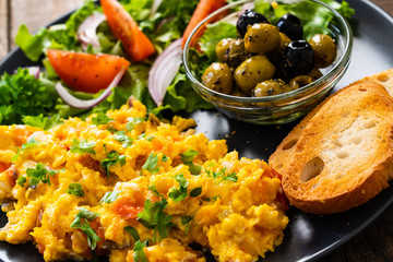 Breakfast - scrambled eggs with vegetables and toasted bread on wooden background