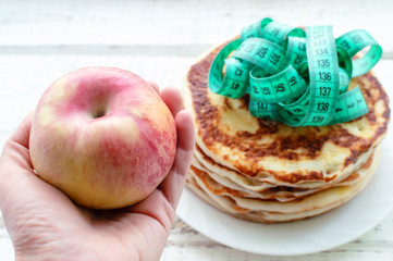 hand holding a red Apple on a background of pancakes with a centimeter tape. the concept of a healthy lifestyle. the fight against excess weight.
