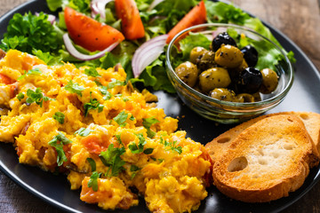 Breakfast - scrambled eggs with vegetables and toasted bread on wooden background